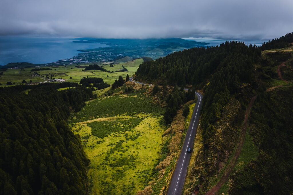 Panoramic landscape of São Miguel with a winding road, lush green vegetation and a partly cloudy sky.