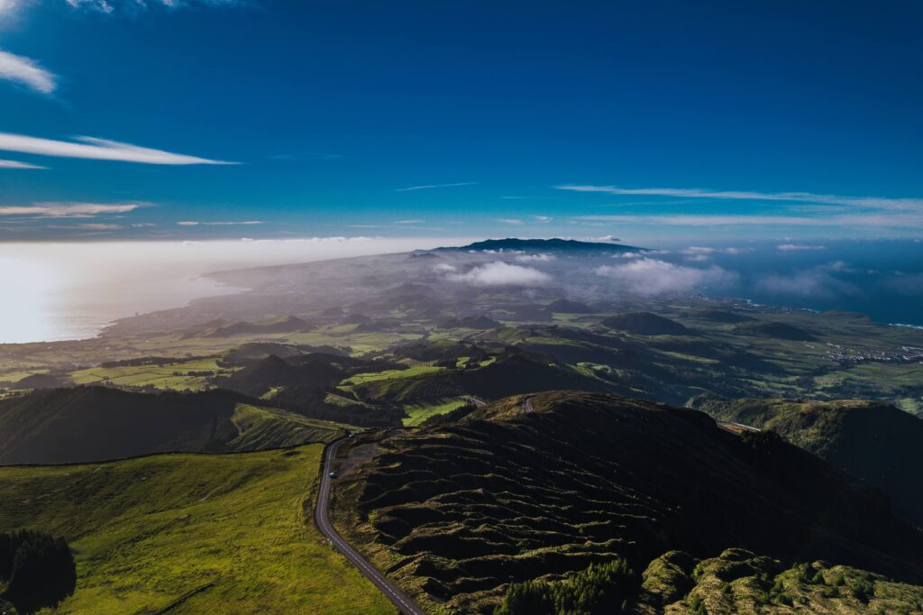 Scenic road in São Miguel surrounded by lush green vegetation, with mountains and mist across the landscape.