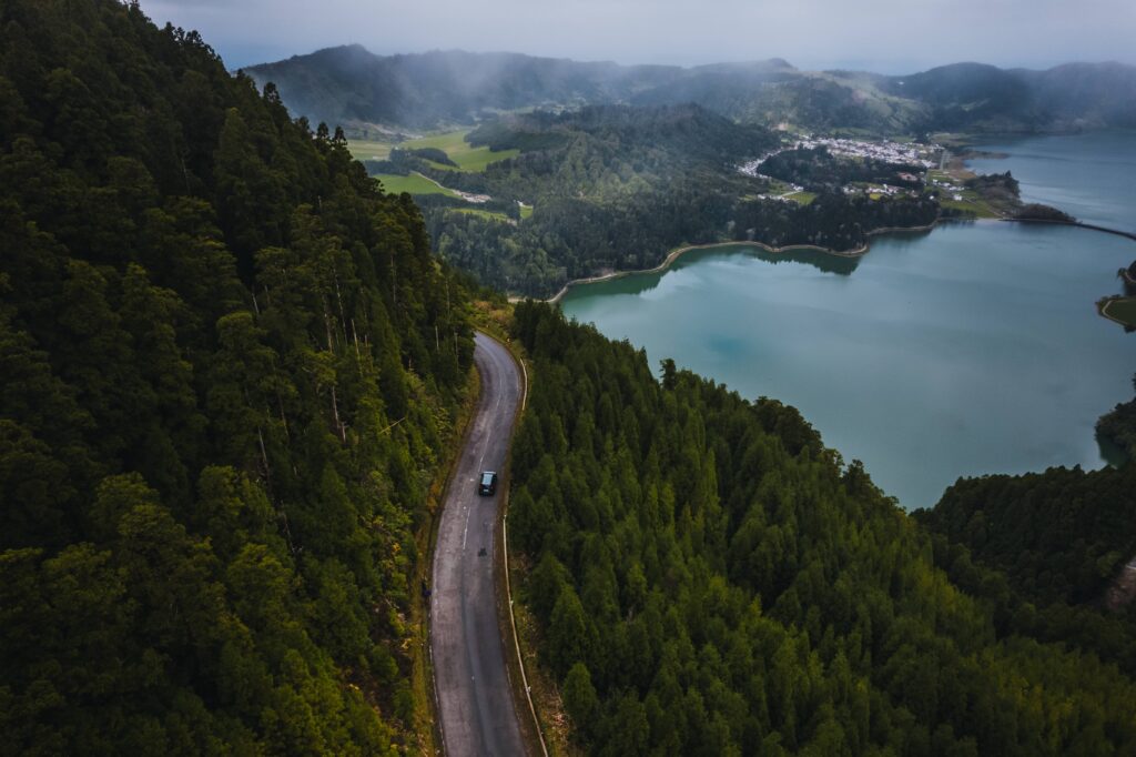 Scenic road in São Miguel surrounded by vegetation, with a volcanic lake in the distance.
