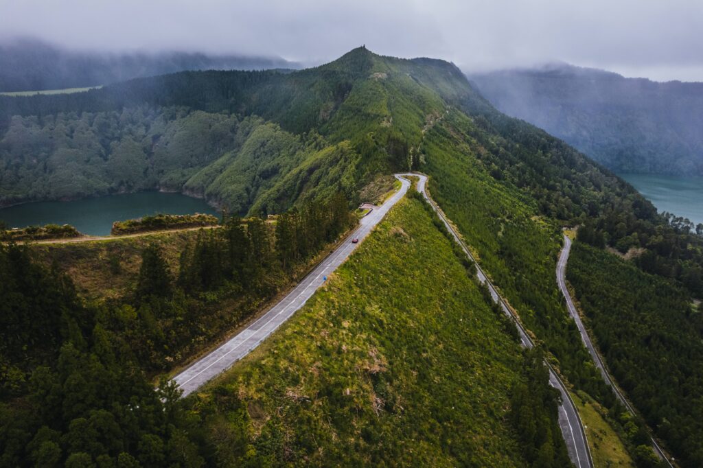 Car travelling along a winding road in São Miguel surrounded by the island's characteristic green landscape.