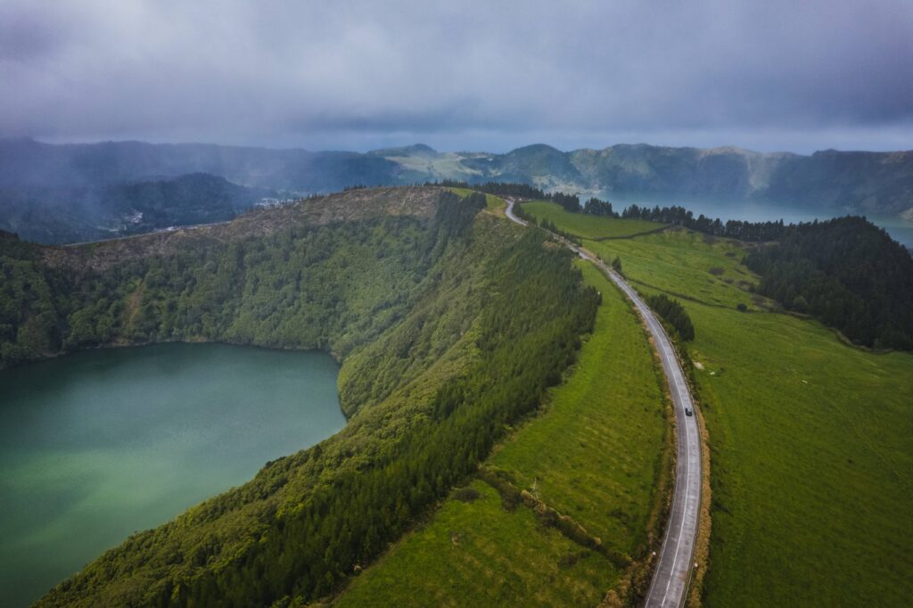 Car on a winding road in São Miguel with volcanic scenery and green vegetation in the background.