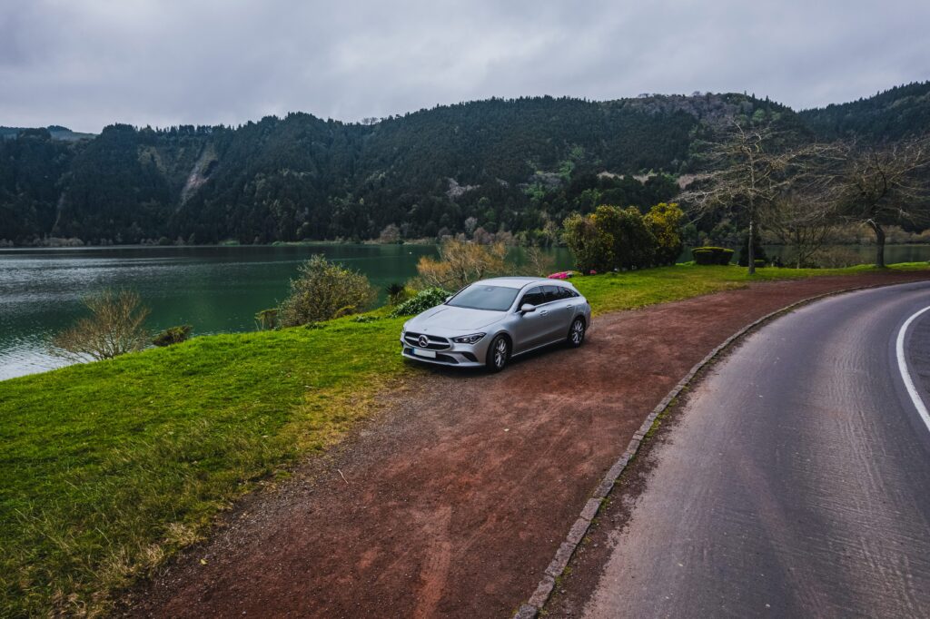 Car on a scenic road in São Miguel surrounded by green vegetation and volcanic scenery.