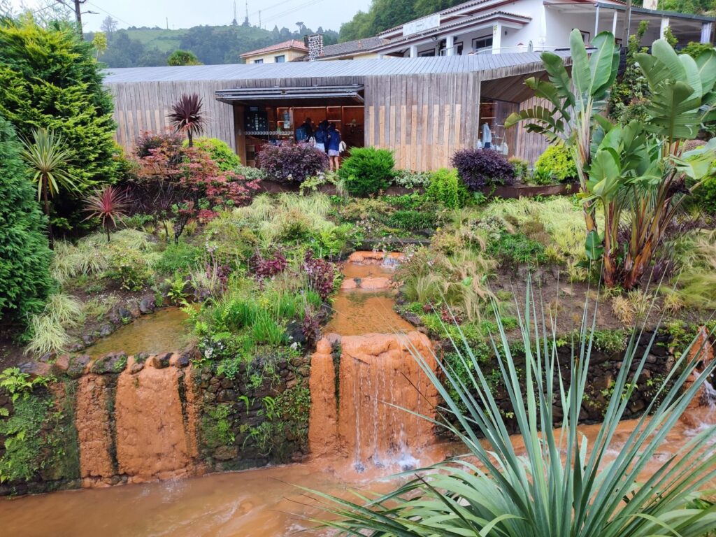 Piscina de águas termais nas Furnas, em São Miguel, envolvida por vegetação e vapor natural.