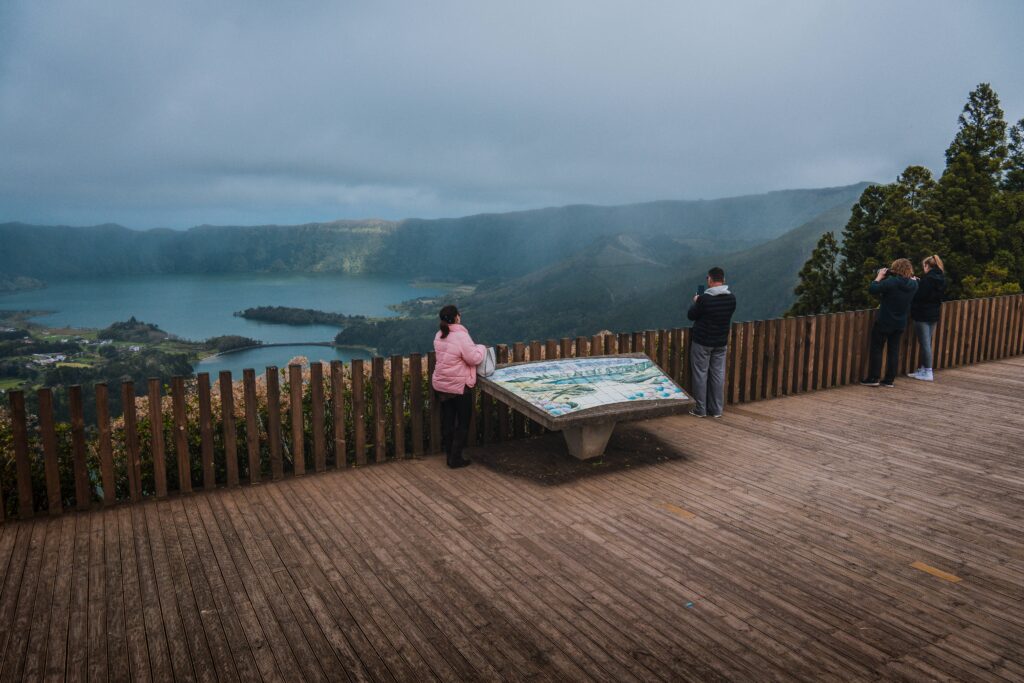 Família com crianças num miradouro de São Miguel a observar uma lagoa e a paisagem envolvente.